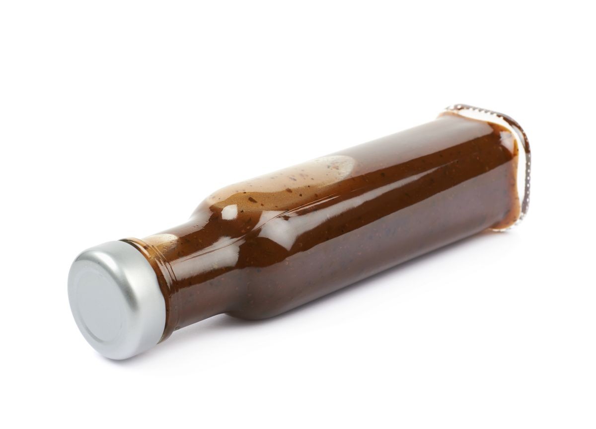 Glass bottle of barbecue bbq sauce lying on its side, composition isolated over the white background